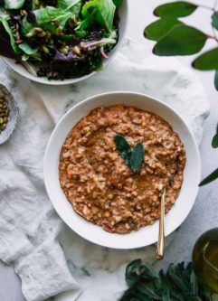 一碗Zuppa di Farro汤在白色桌子上，带有鼠尾草休假，装饰，金勺和白色餐巾纸